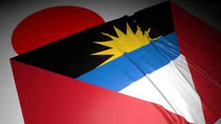 Antigua-and-Barbuda National Flag, The national flag placed on top of the Japanese flag on a desk in a dark space