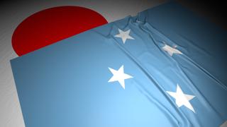 Federated-States-of-Micronesia National Flag, The national flag placed on top of the Japanese flag on a desk in a dark space