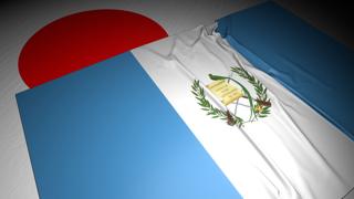 Guatemala National Flag, The national flag placed on top of the Japanese flag on a desk in a dark space