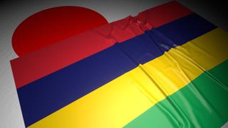 Mauritius National Flag, The national flag placed on top of the Japanese flag on a desk in a dark space