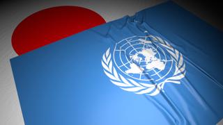 国連(UN)国旗, 暗い空間の中の机の上の日本の国旗の上に置かれた国旗