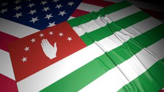 Abkhazia National Flag, A flag placed on top of an American flag on a desk in a dark space