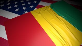 Guinea National Flag, A flag placed on top of an American flag on a desk in a dark space