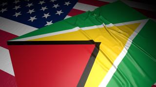 Guyana National Flag, A flag placed on top of an American flag on a desk in a dark space