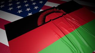 Malawi National Flag, A flag placed on top of an American flag on a desk in a dark space