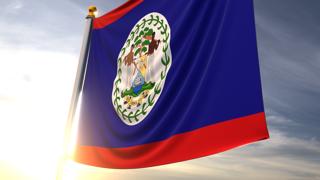 Belize National Flag, A fluttering flag and flagpole seen up close against a dark blue sky